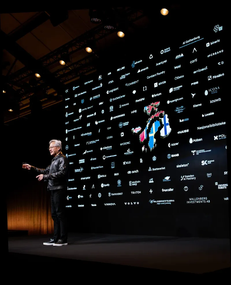 Speaker on stage in front of screen with numerous company logos.