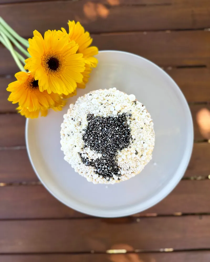 A cake decorated with the GitHub logo in black and white sprinkles, with yellow daisy flowers next to it